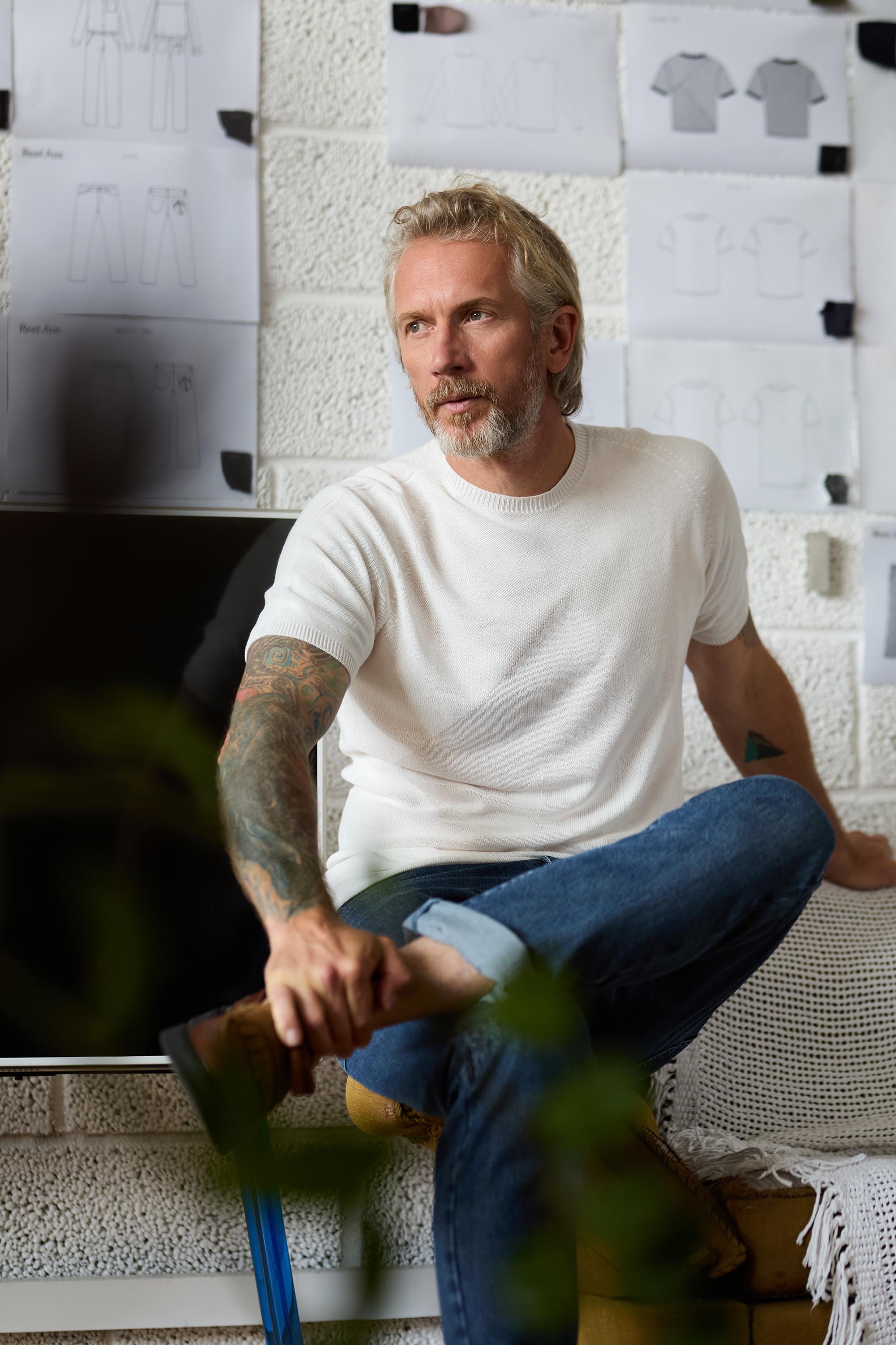 A person in a white knit shirt seated in front of garment sketches